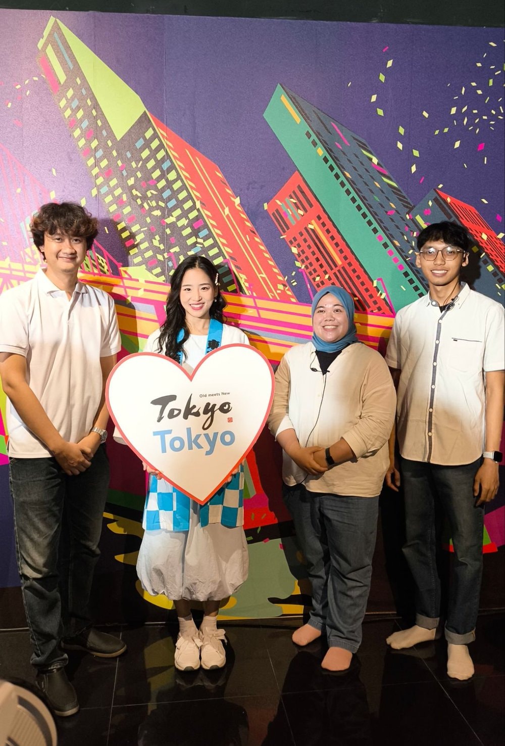 Tim berfoto di depan backdrop ilustrasi gedung-gedung Tokyo, bintang tamu memegang papan berbentuk hati bertuliskan Tokyo Tokyo Old meets New