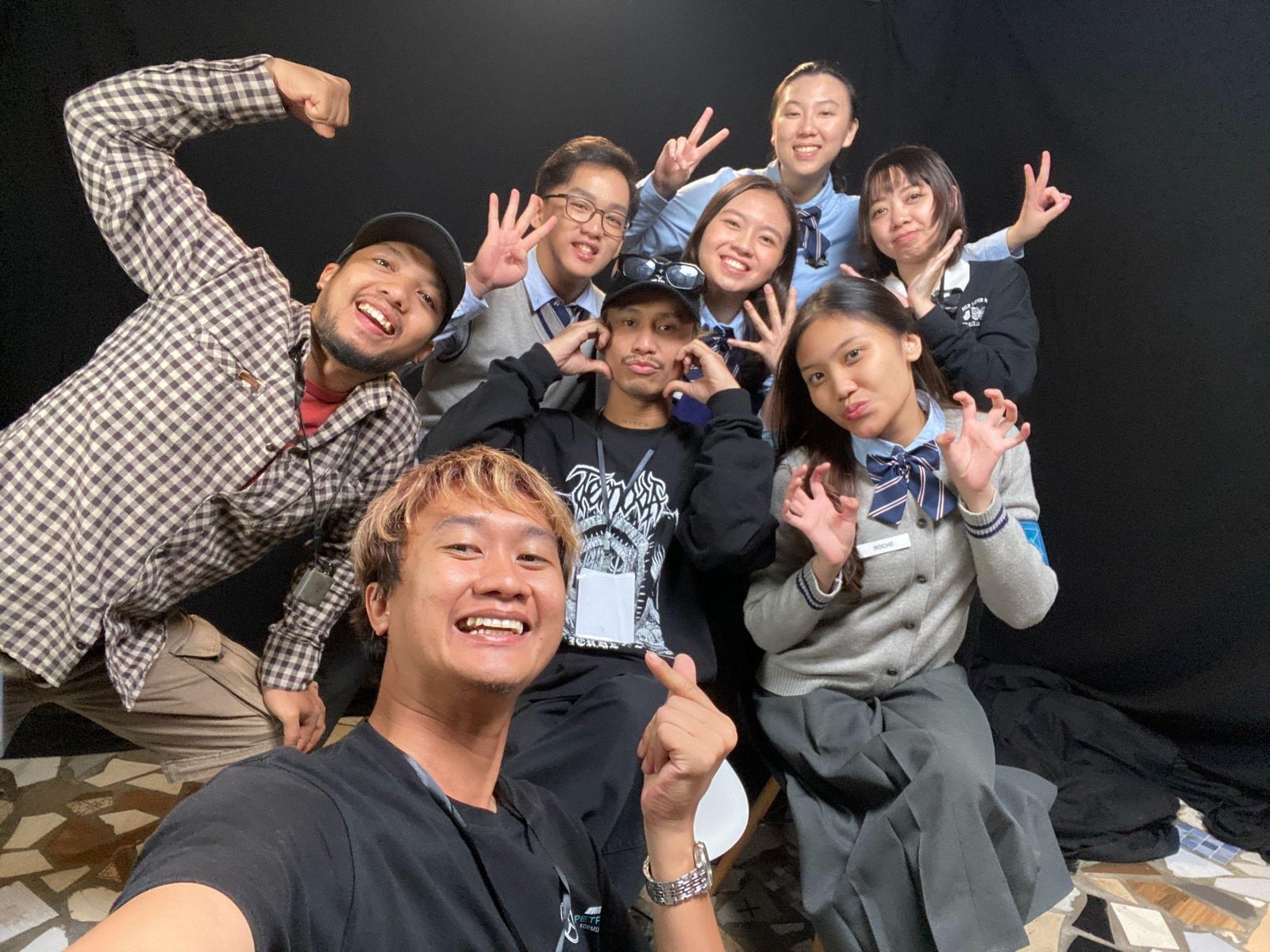 Foto selfie bersama tim produksi dan peserta berseragam sekolah di lokasi syuting dengan latar belakang gelap, semua berpose ceria