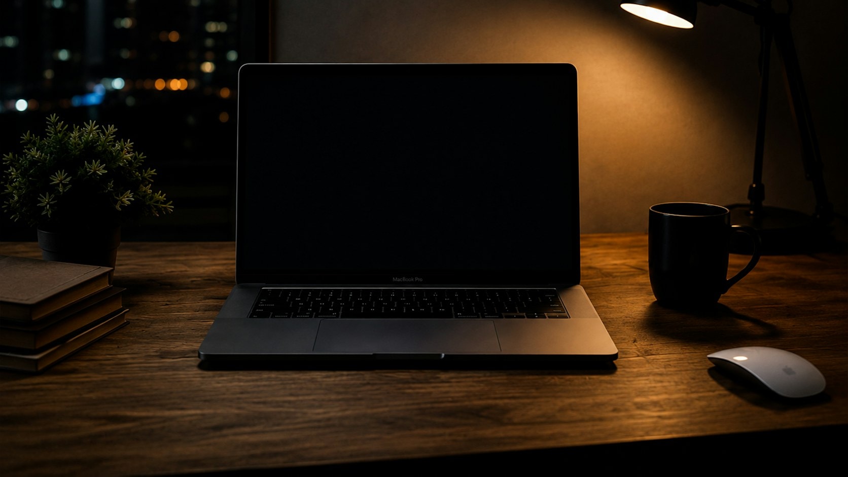 A desk at night with a laptop, a desk lamp, and a city view