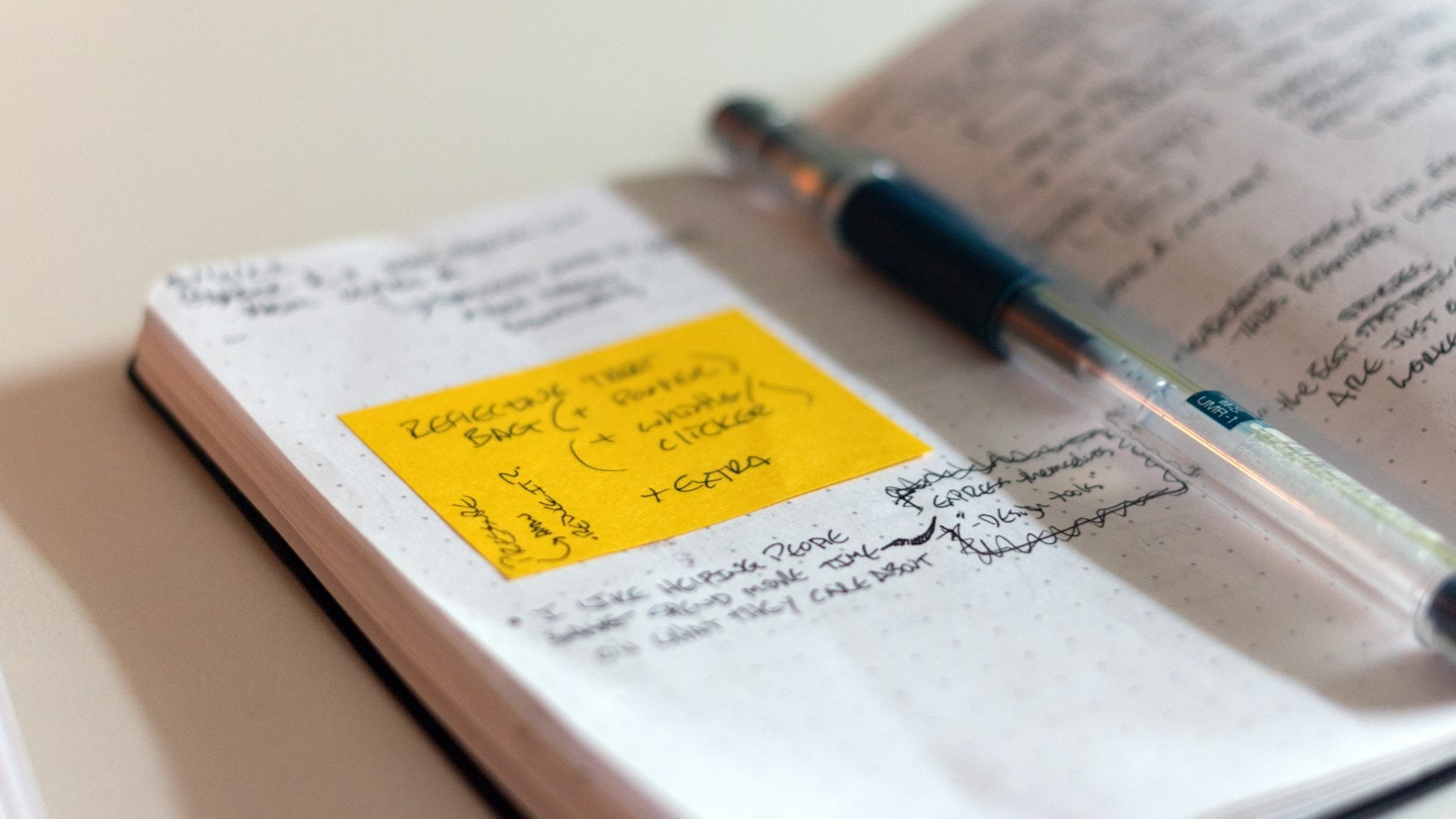 An open notebook with handwritten notes and a yellow sticky note, with a pen on top