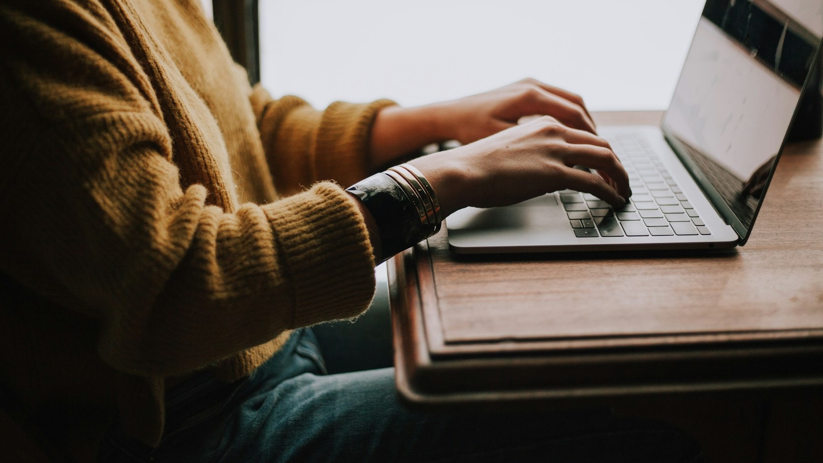 Seseorang mengetik di laptop di meja kayu