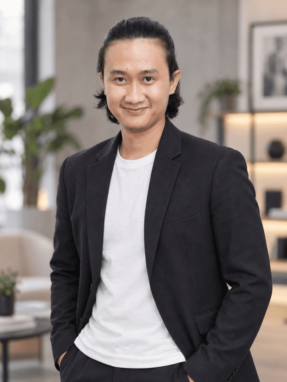Hasil AI gaya agensi kreatif: pria yang sama memakai blazer hitam dengan kaus putih polos, berdiri di studio kreatif minimalis dengan tanaman dan rak yang blur