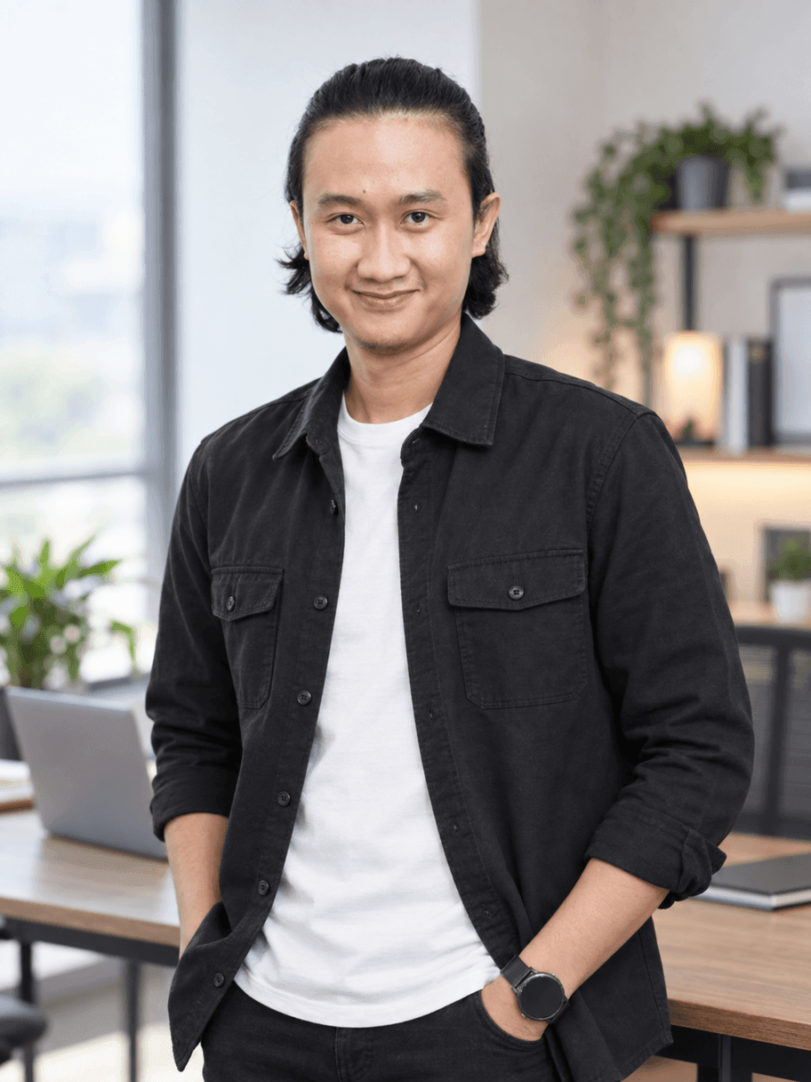Hasil AI gaya founder: pria yang sama memakai overshirt hitam dengan kaus putih dan jam tangan, berdiri di ruang kerja dengan laptop, rak, dan jendela besar yang blur
