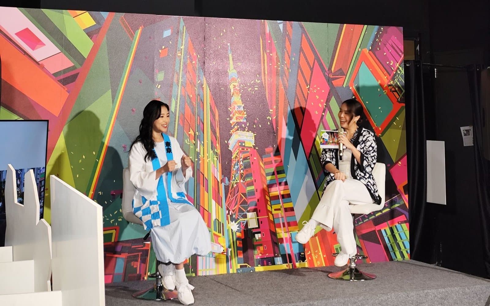 Talkshow press conference Walk Tokyo di panggung dengan backdrop ilustrasi kota Tokyo dan Tokyo Tower, bintang tamu berbaju happi biru putih berbincang dengan MC